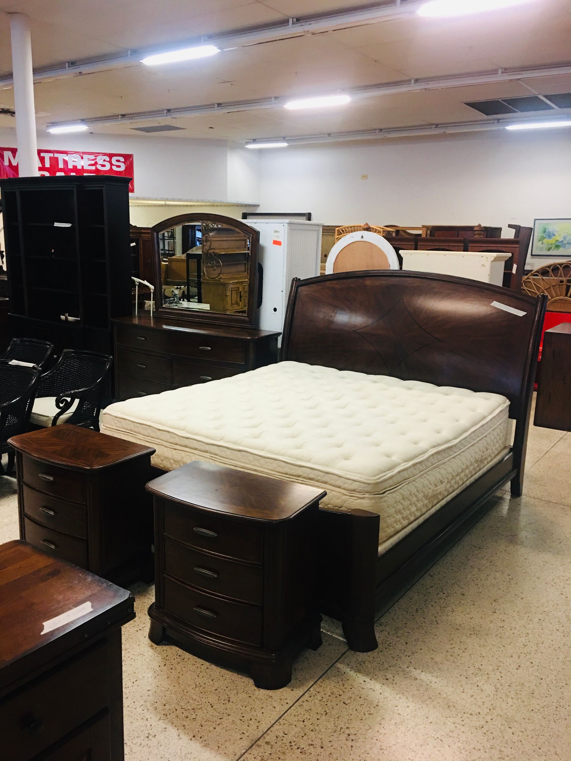 A dark wood sleigh bed with a white mattress and two matching nightstands in a furniture store showroom.