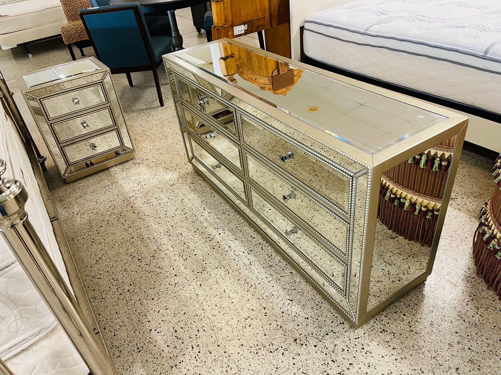 A mirrored dresser and matching nightstand with gold-tone frames displayed in a furniture showroom with terrazzo floors.