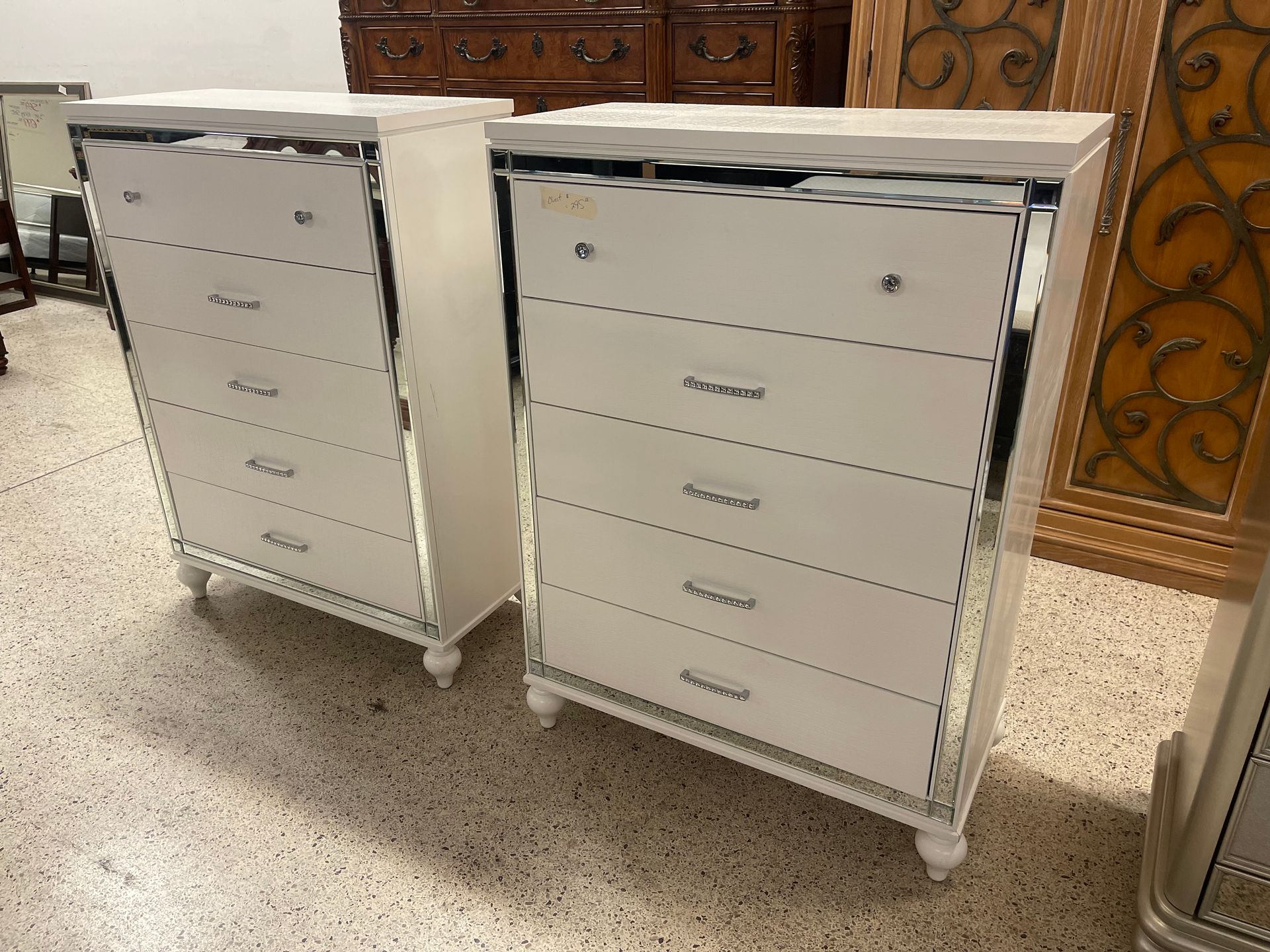 Two white five-drawer dressers with mirrored side accents, sitting on a speckled floor.
