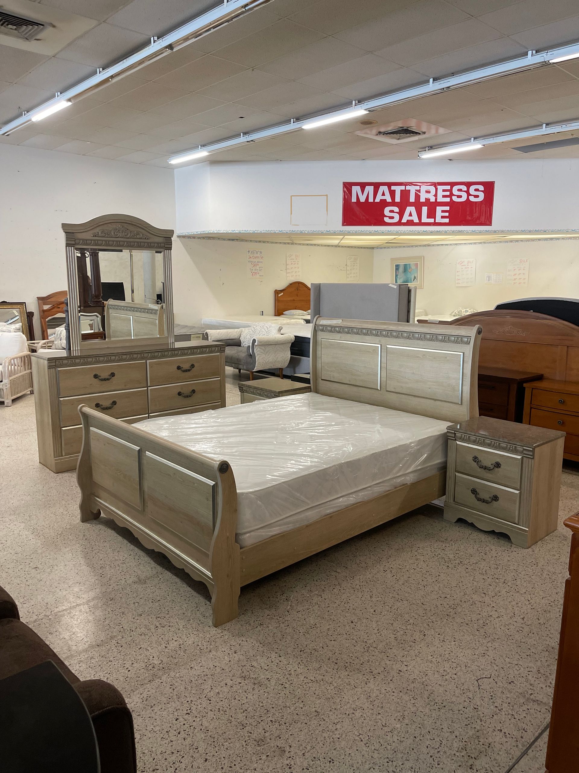 A light-wood bedroom set with a bed, dresser with mirror, and nightstand in a furniture store.