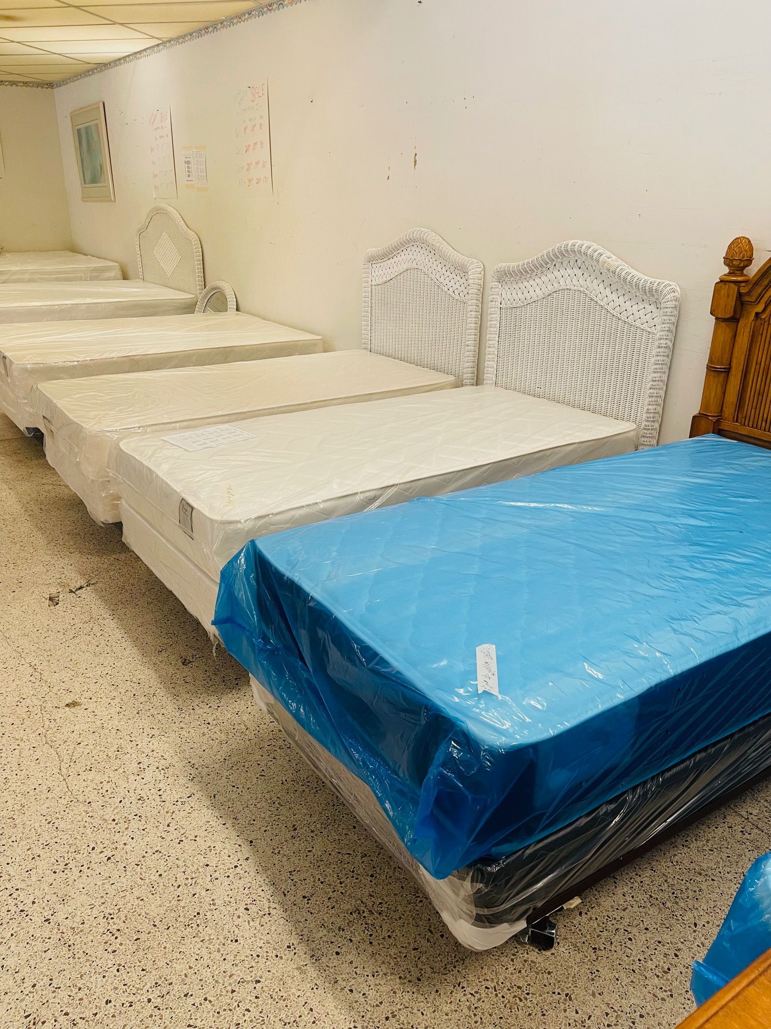 Beds in a room. Multiple beds with white and blue mattresses in a row against a white wall.