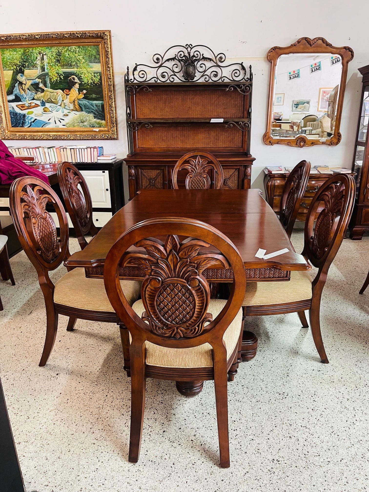 A dining set with an ornate wooden table and chairs featuring pineapple carvings, arranged in a showroom.
