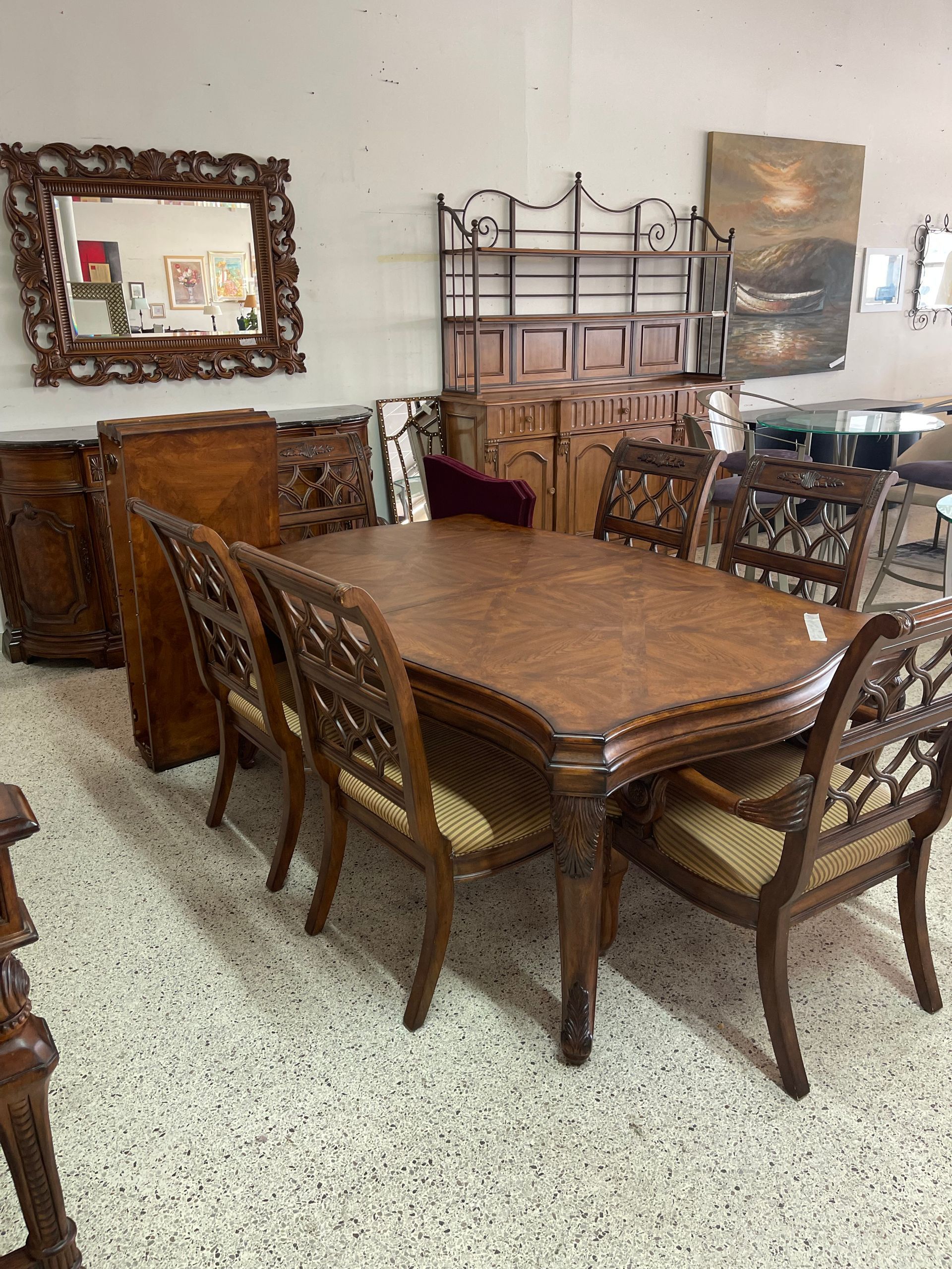 A dark wood dining set featuring an ornate table and chairs with lattice backs, placed in a showroom with a wall mirror.