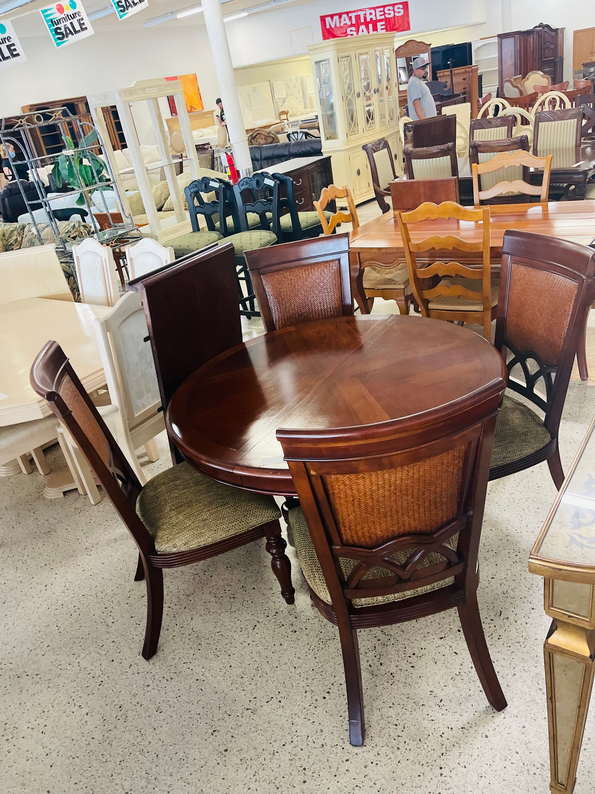 A round, dark wood dining table with four matching chairs featuring patterned seats, displayed in a furniture store.