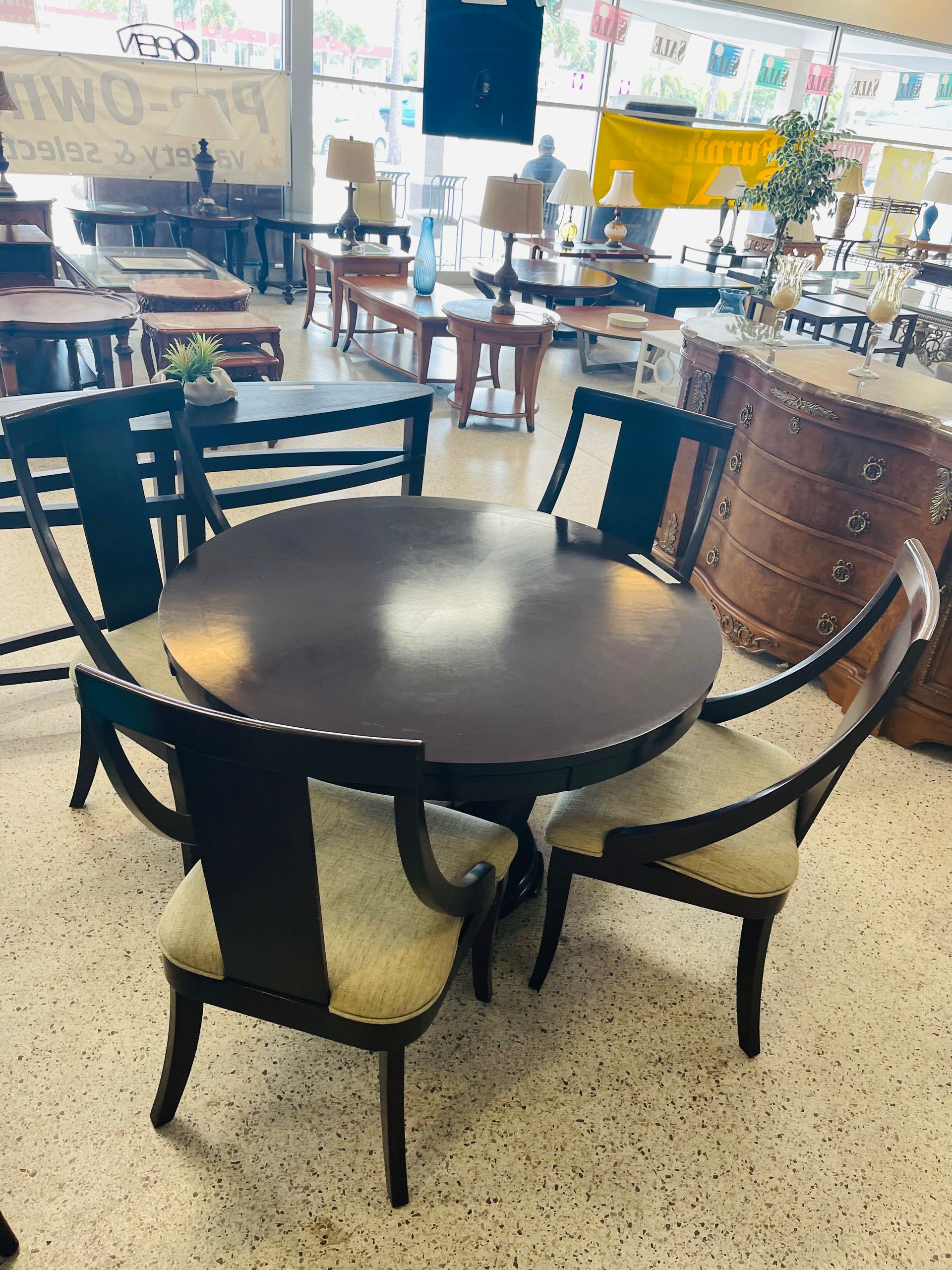 A circular dark wood dining table with four matching chairs featuring cream-colored upholstered seats in a furniture store.