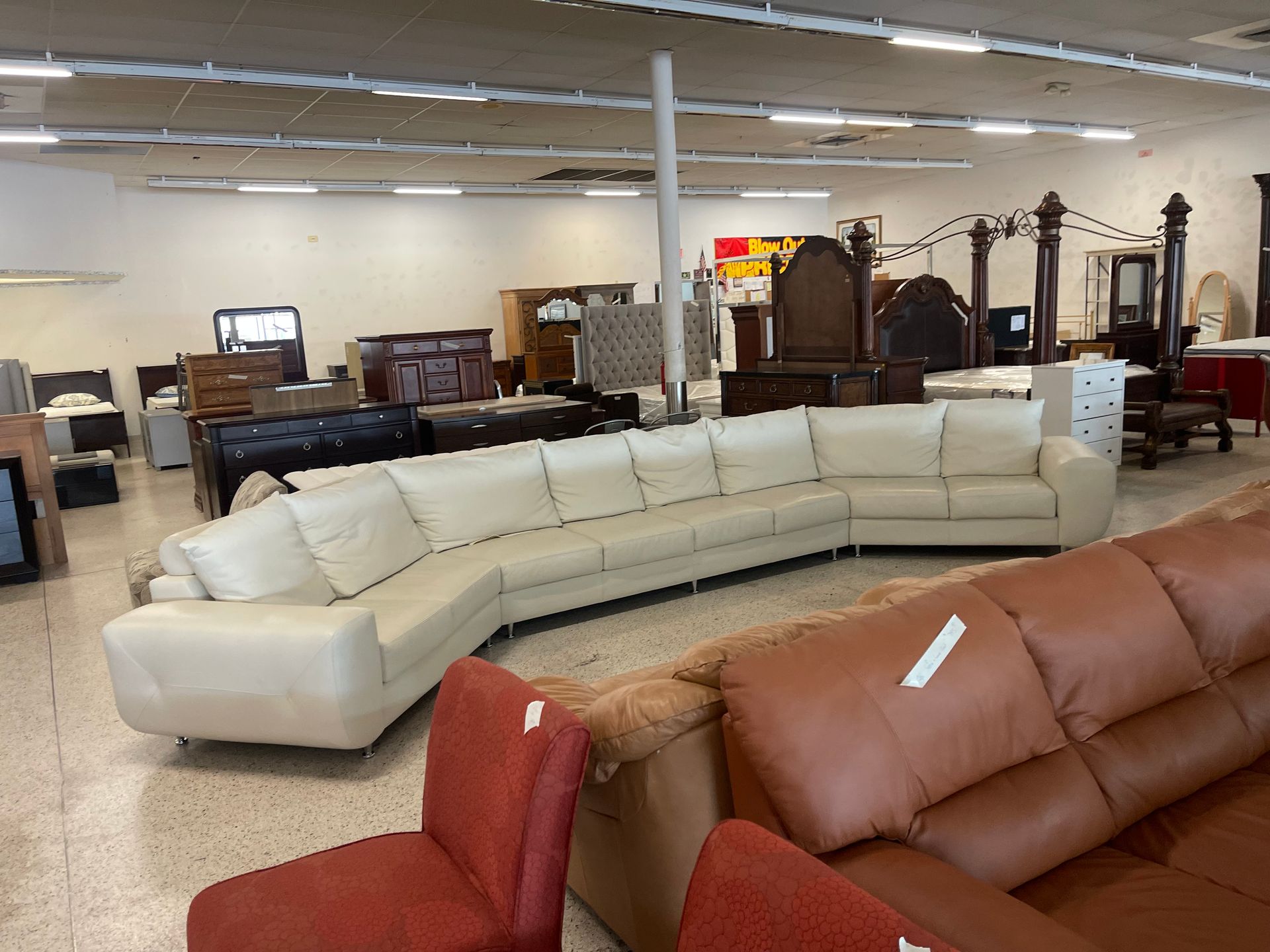 Large white leather sectional sofa displayed in a furniture store with other beds and couches in the background.
