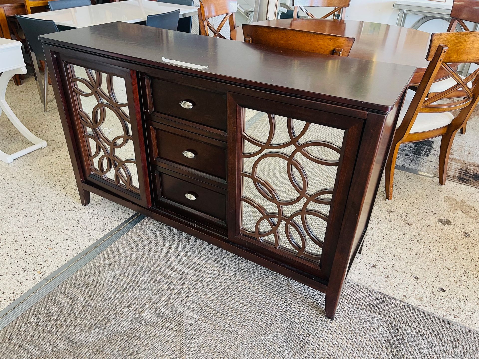 A dark wood sideboard featuring three central drawers flanked by two cabinet doors with decorative circular metal inlays.