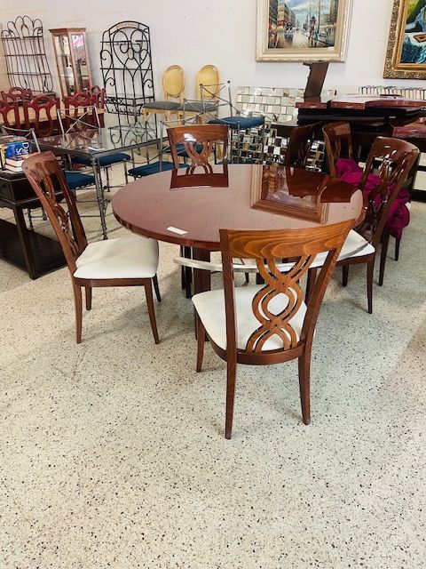 A round, wood-toned dining table surrounded by four wooden chairs with distinctive interlocking-loop backs and white seats.