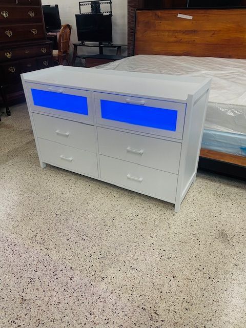A white, six-drawer dresser with blue LED lights on the top two drawers, displayed in a furniture showroom.