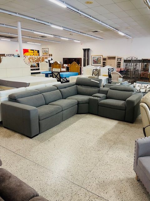 A gray modular sectional sofa with a built-in console sits on a speckled floor inside a brightly lit furniture store.