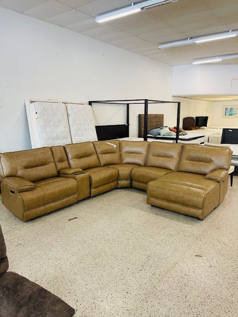 A tan leather sectional sofa with recliners and a chaise lounge on display in a brightly lit furniture store.