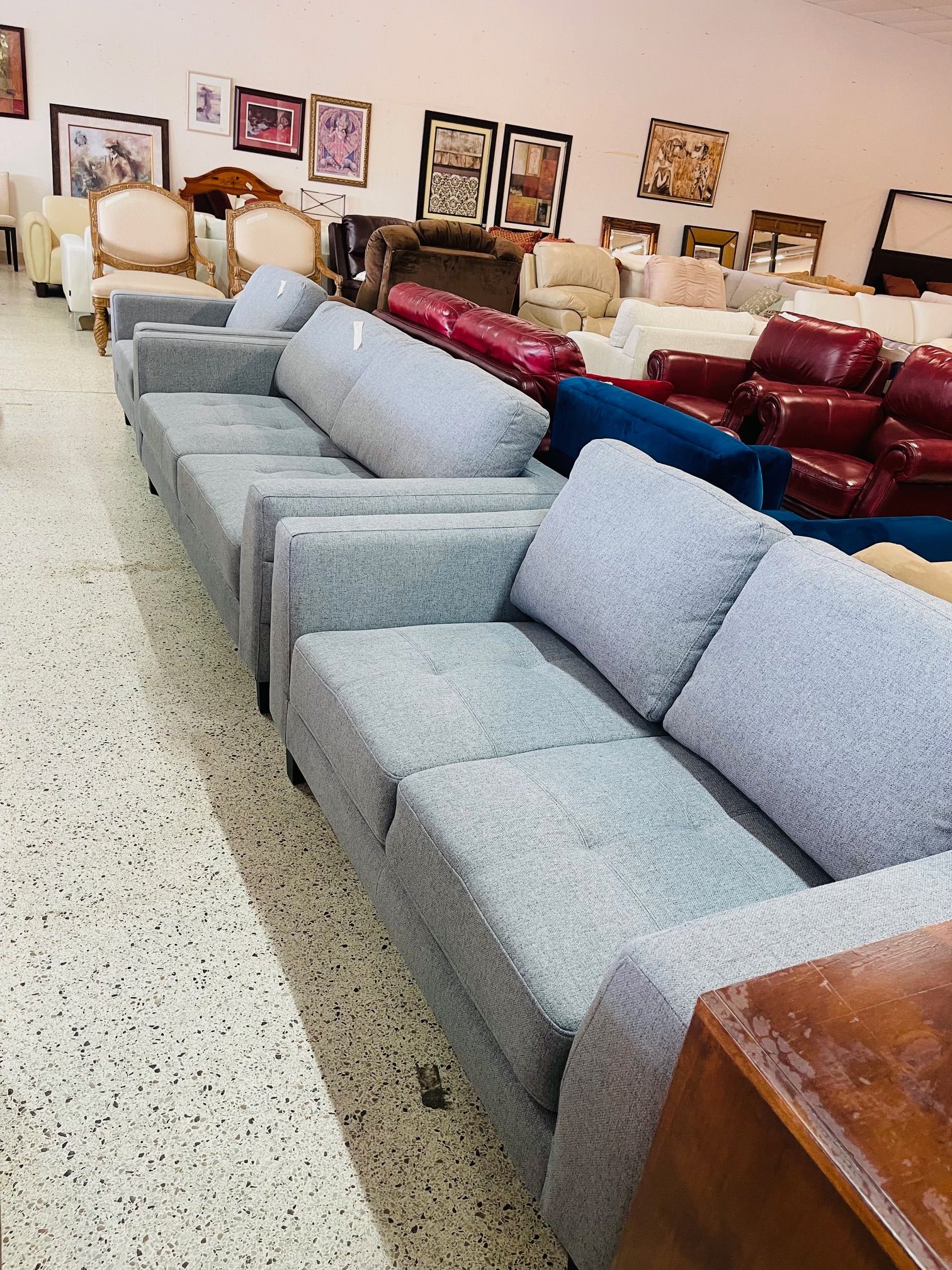 Row of grey fabric sofas in a furniture store showroom with other chairs and wall art visible in the background.
