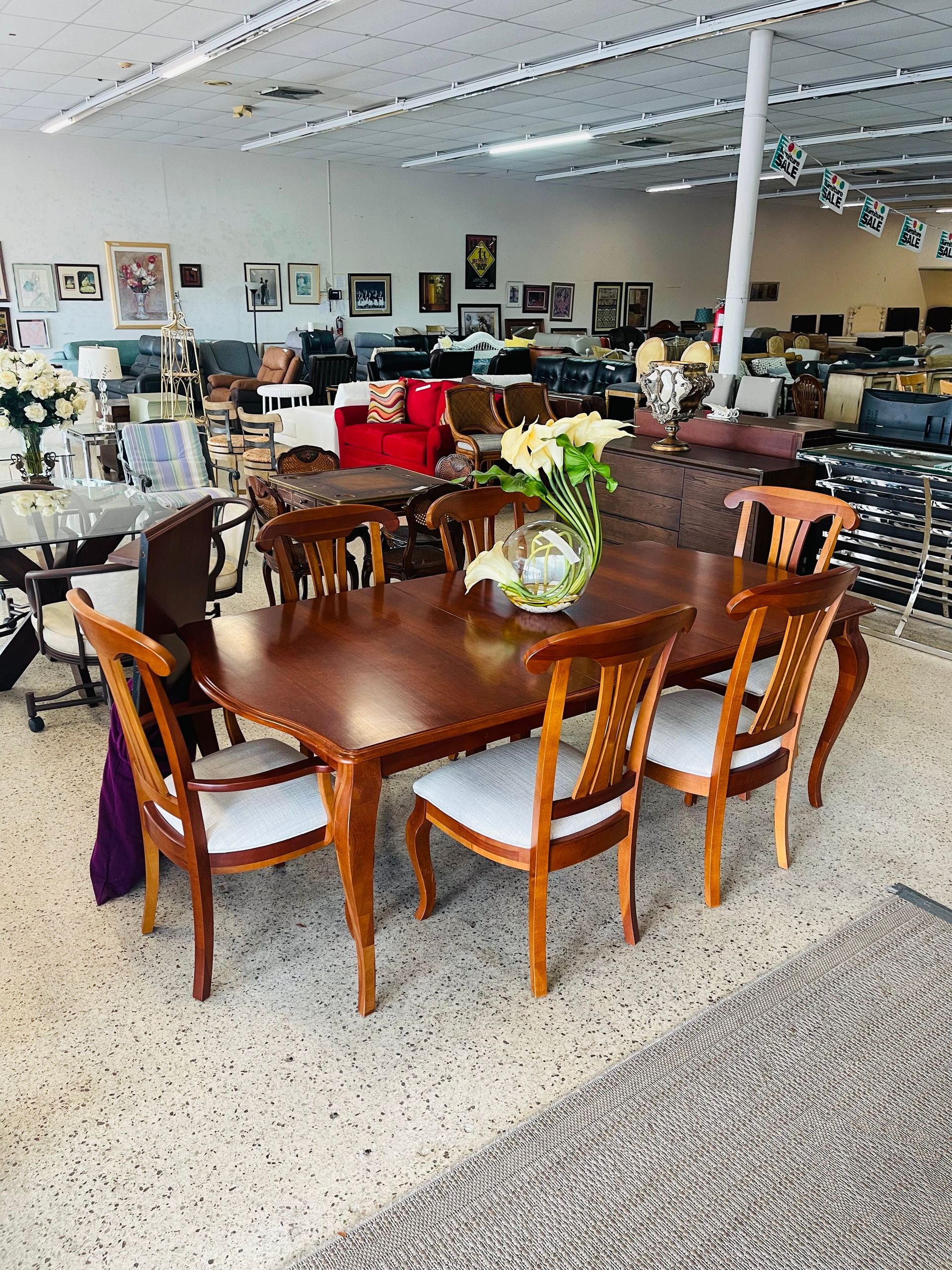 A dining room set with a wooden table and six chairs with white cushions sits on a speckled floor inside a store.