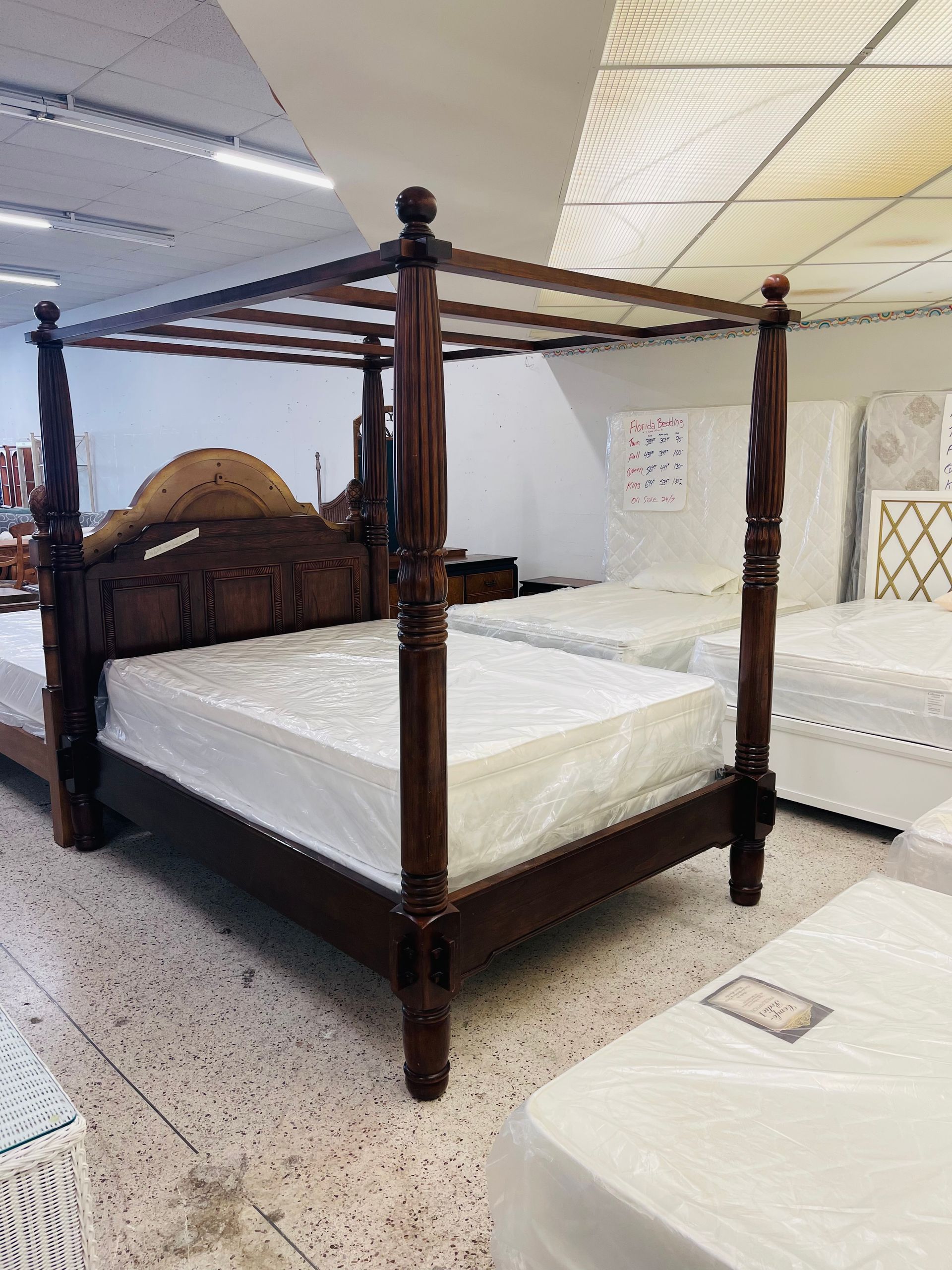 A dark wood four-poster bed with a white mattress in a furniture store.