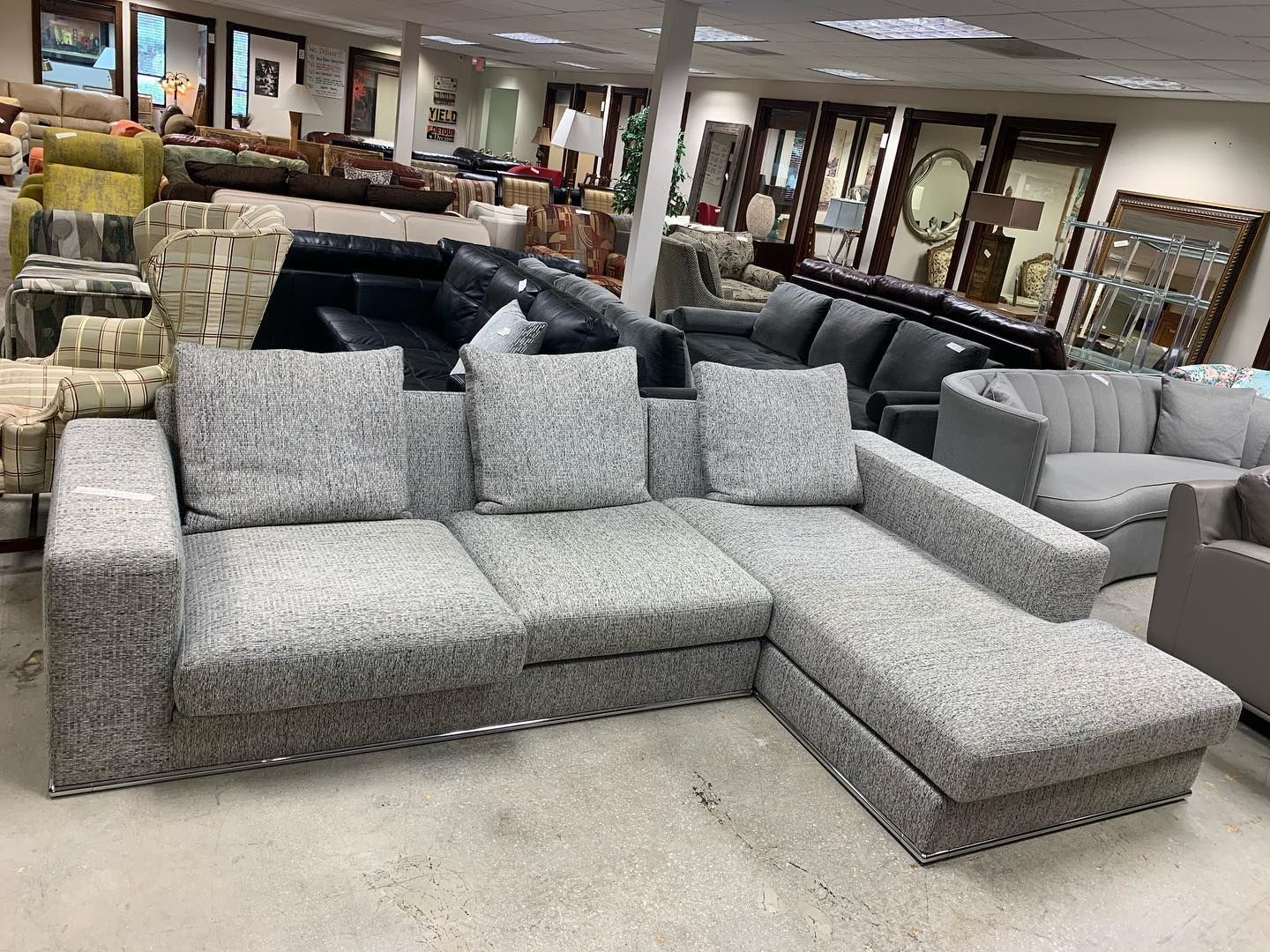 A gray, speckled fabric sectional sofa with a chaise lounge sits in a brightly lit furniture showroom.