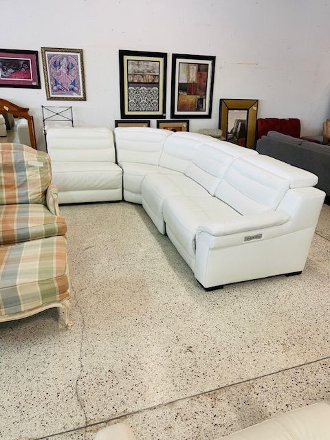 A large white leather sectional sofa in a showroom, with framed art on the wall behind and a plaid chair to the left.