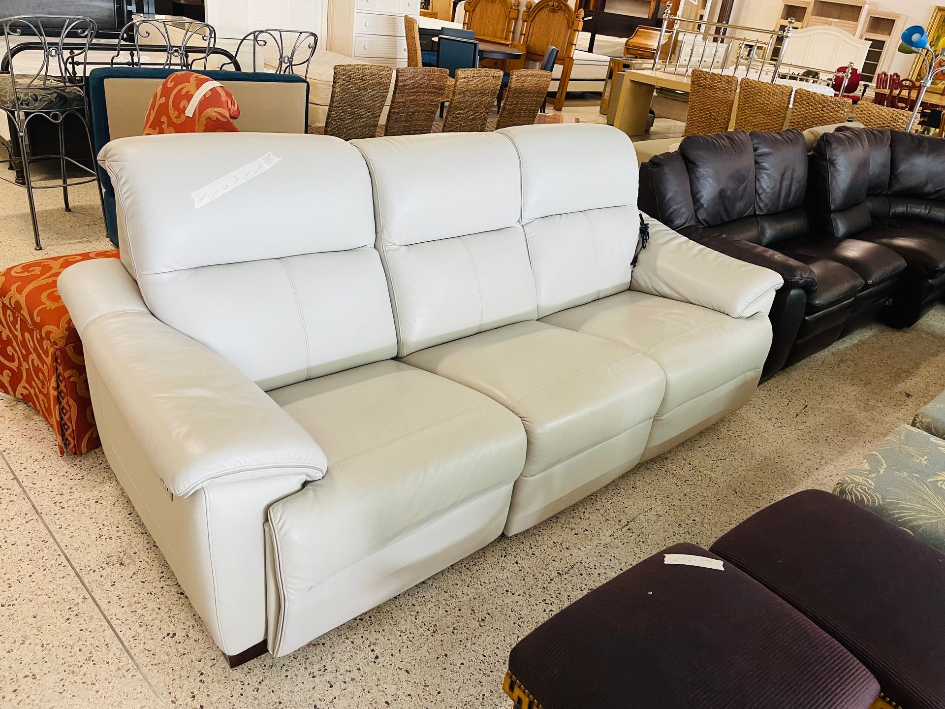 A light grey leather reclining sofa sits on a tiled floor in a furniture store, near a dark brown sofa.