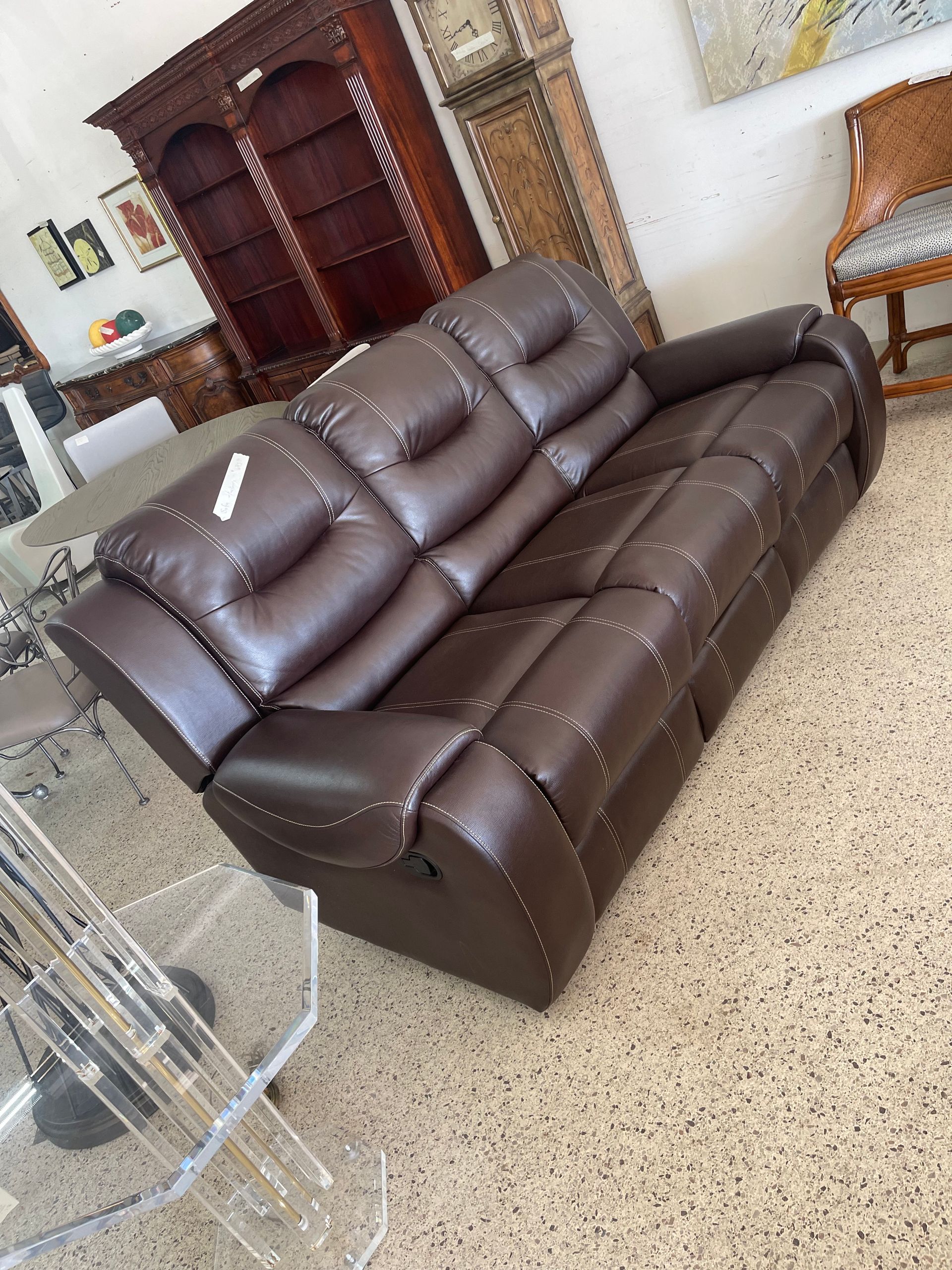 A brown leather reclining sofa with decorative nailhead trim, displayed in a furniture showroom.