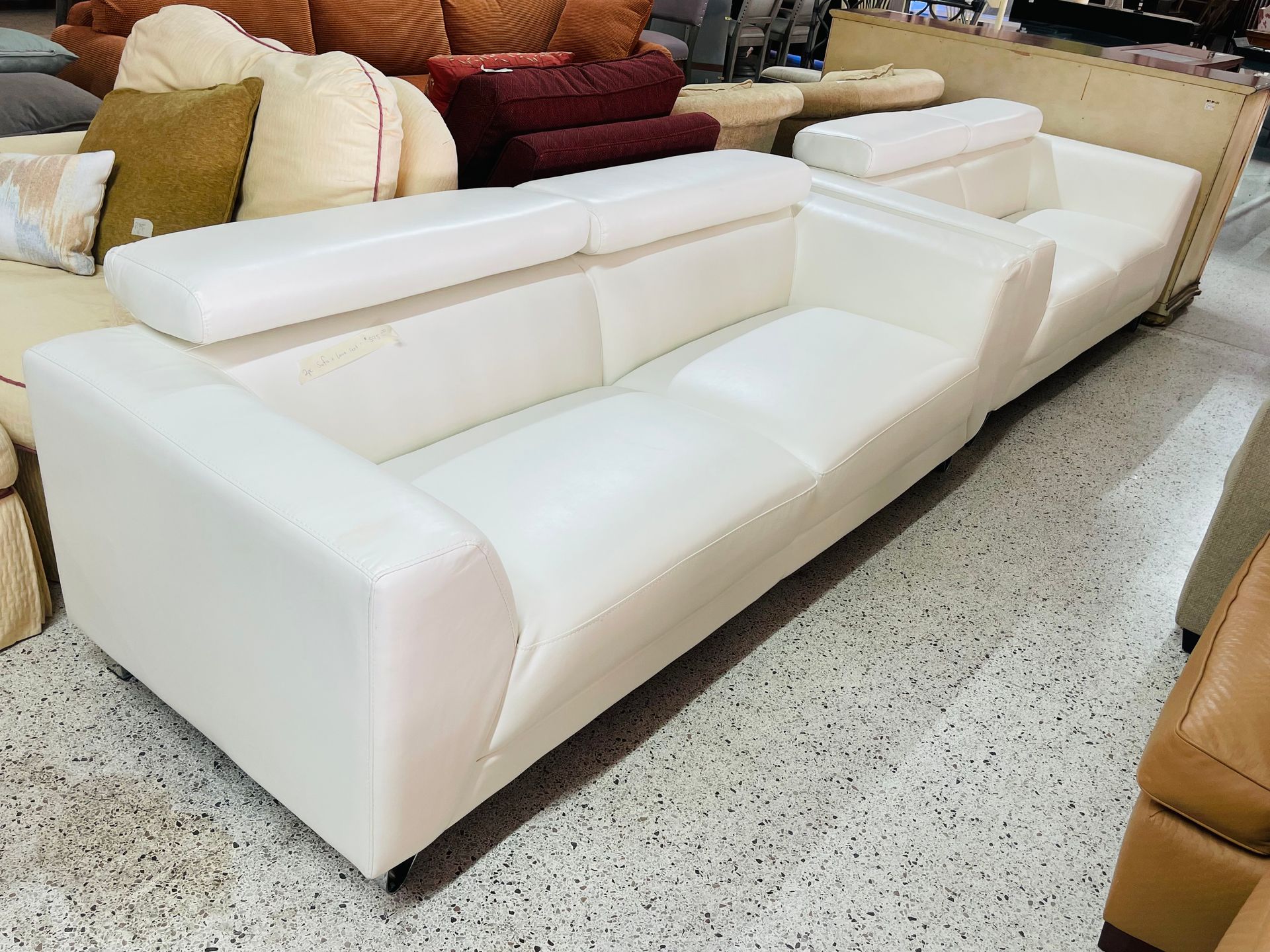 A modern, white leather sofa with adjustable headrests in a showroom setting with a terrazzo floor.