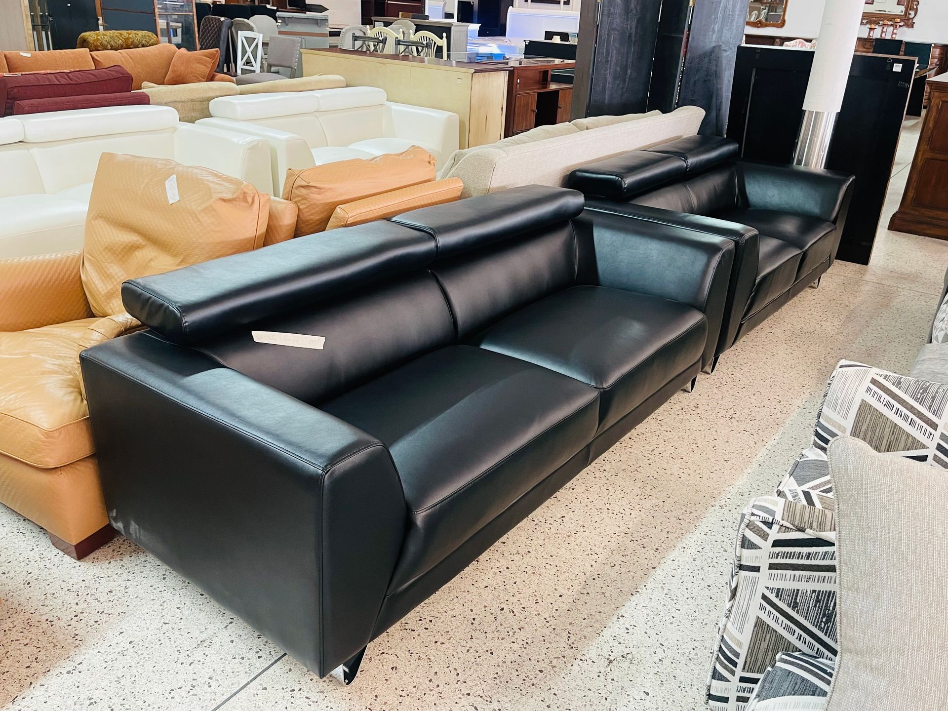 A row of modern sofas for sale in a showroom, featuring a prominent black leather couch in the foreground.