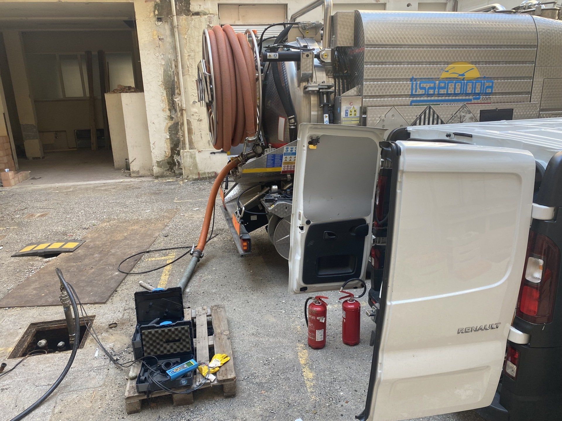 Un camion per la pulizia delle fogne parcheggiato vicino a un tombino, con le portiere e l'attrezzatura aperte.