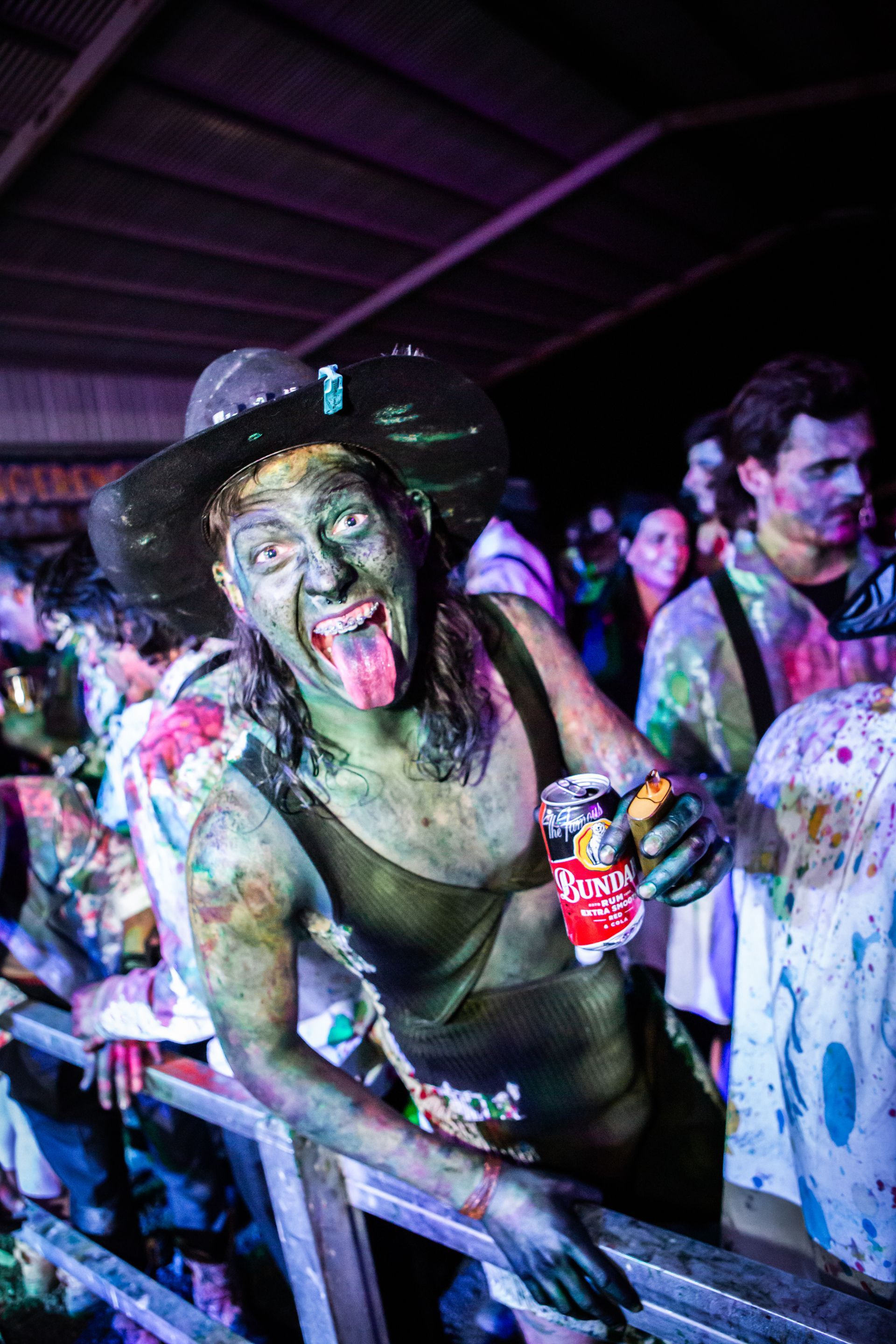 A woman with green paint on her face is holding a can of bud light