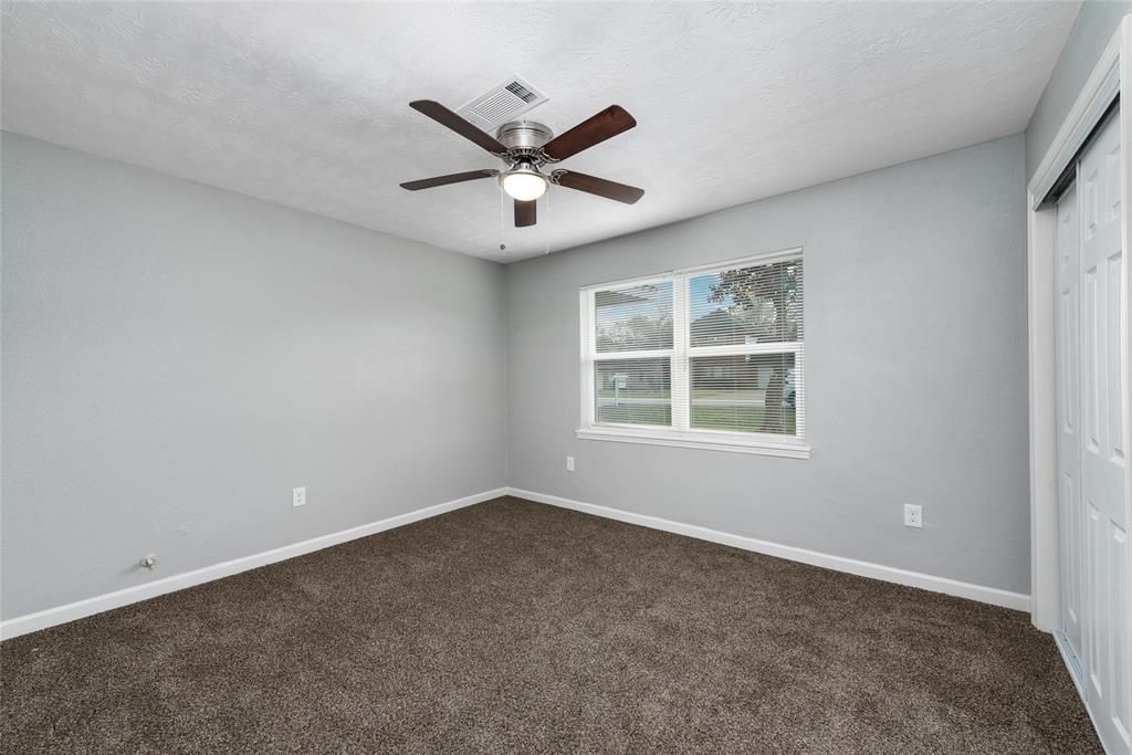 An empty bedroom with a ceiling fan and two windows.