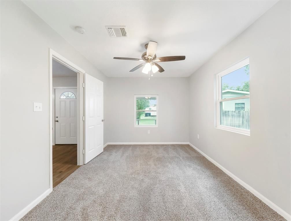 An empty room with a ceiling fan and two windows.