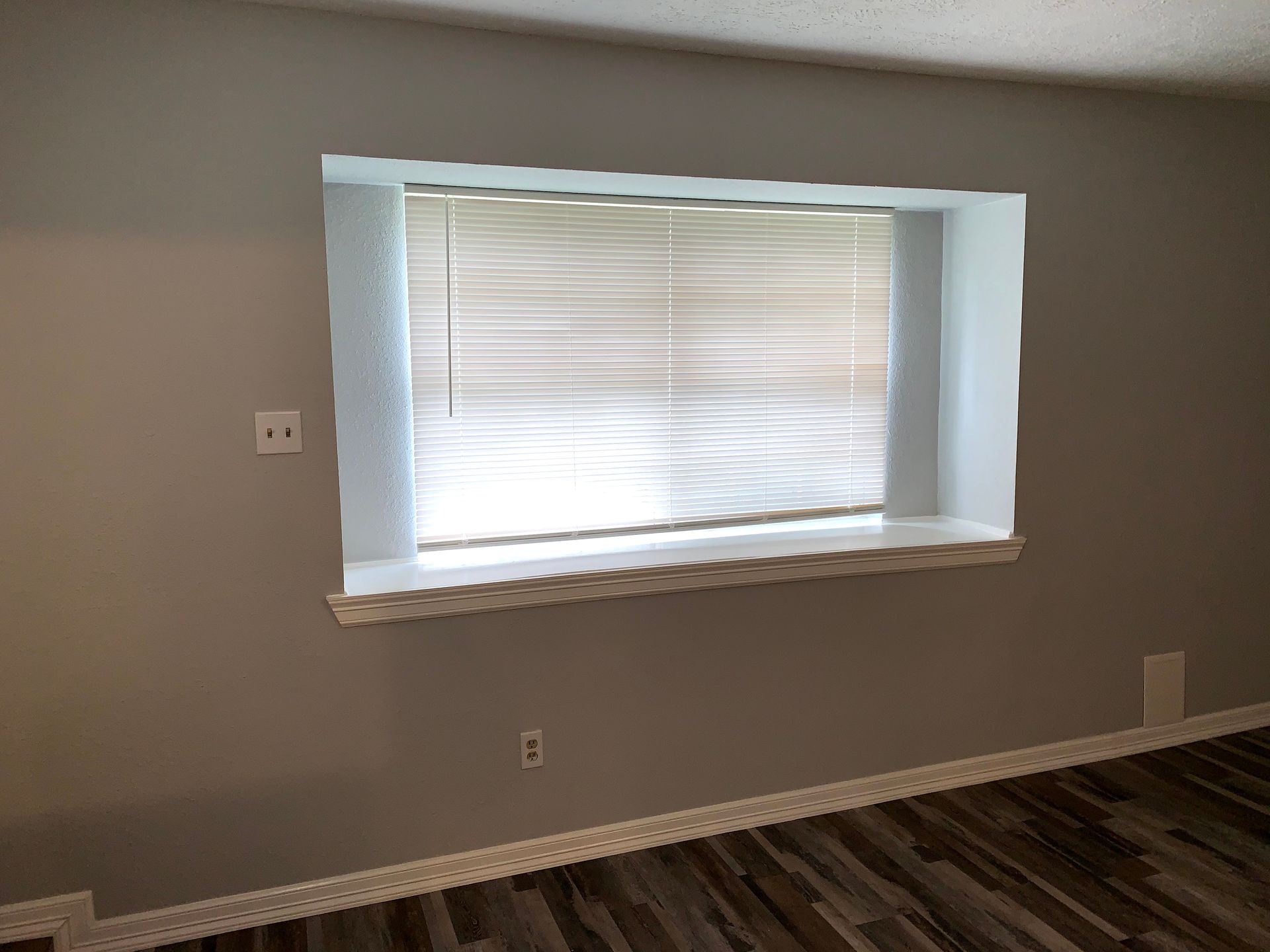 An empty living room with a large window and blinds.