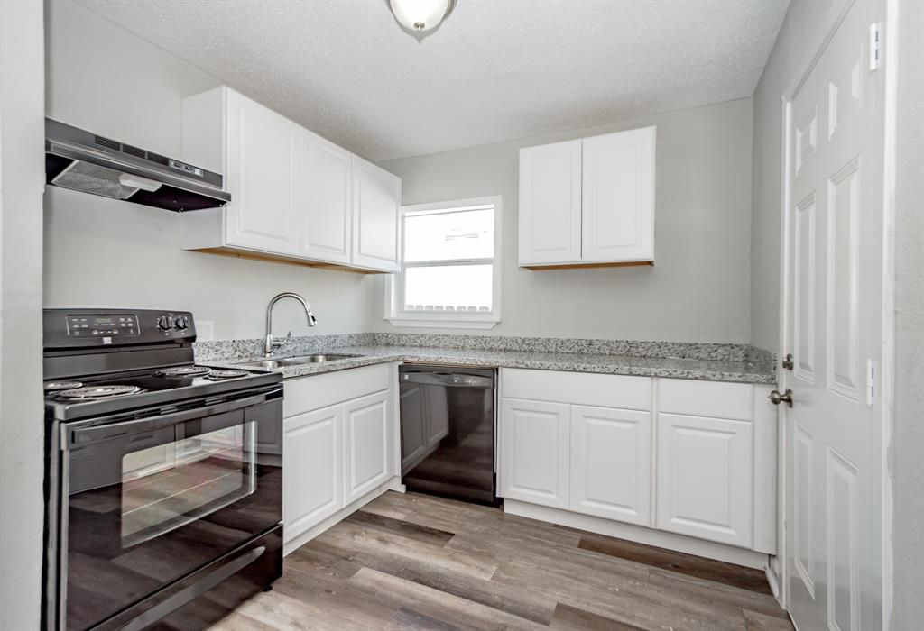A kitchen with white cabinets , a black stove , a sink , and a window.