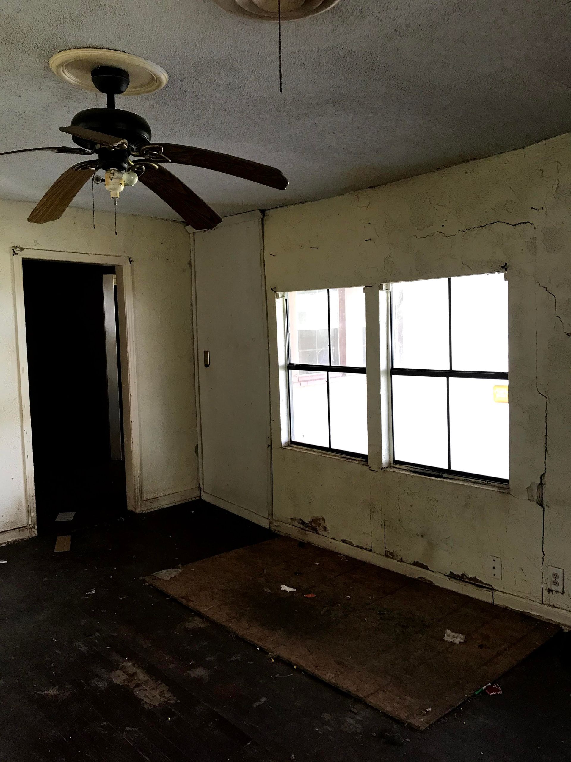 An empty room with a ceiling fan and two windows