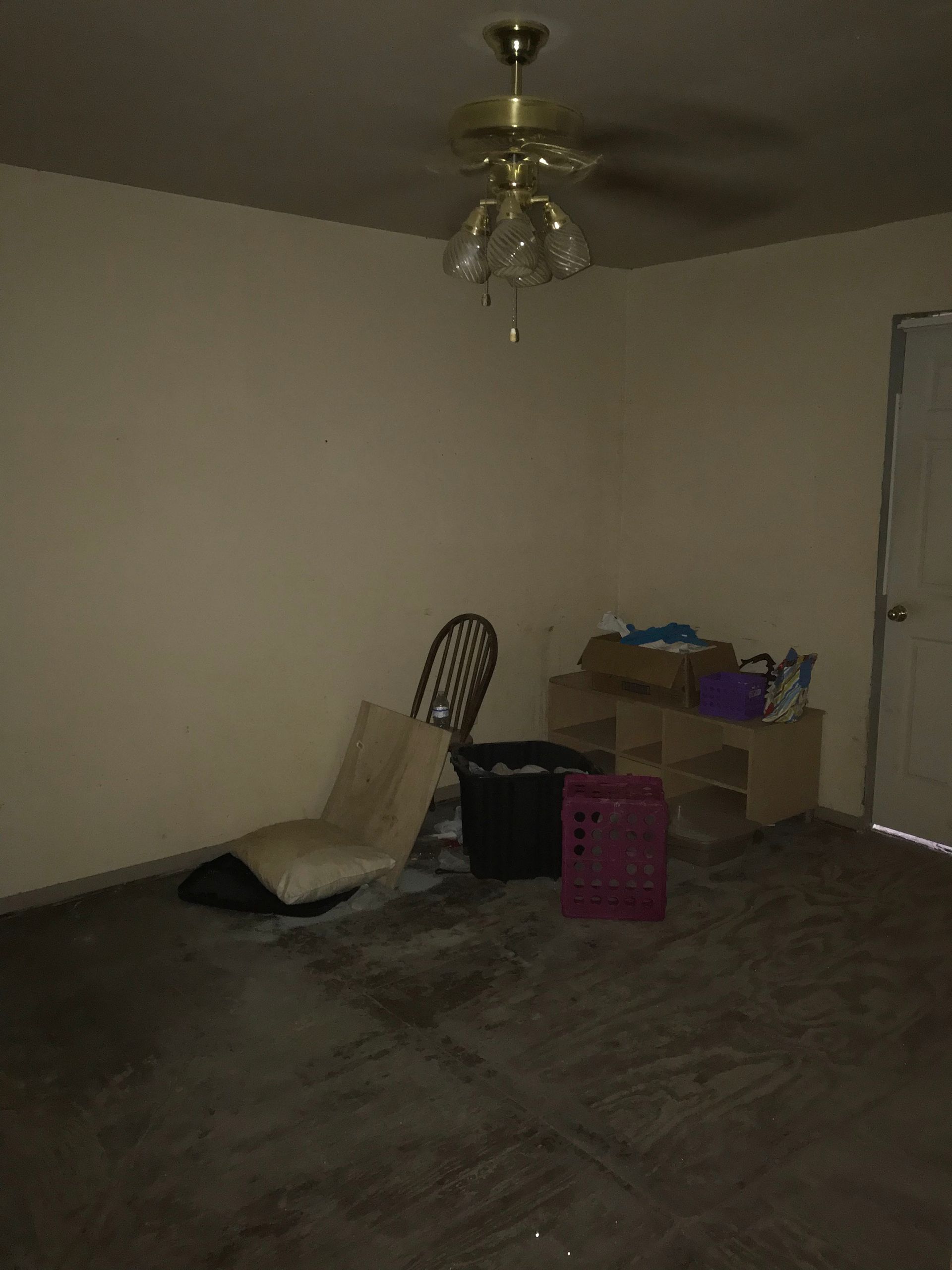 An empty living room with a ceiling fan and a chair.