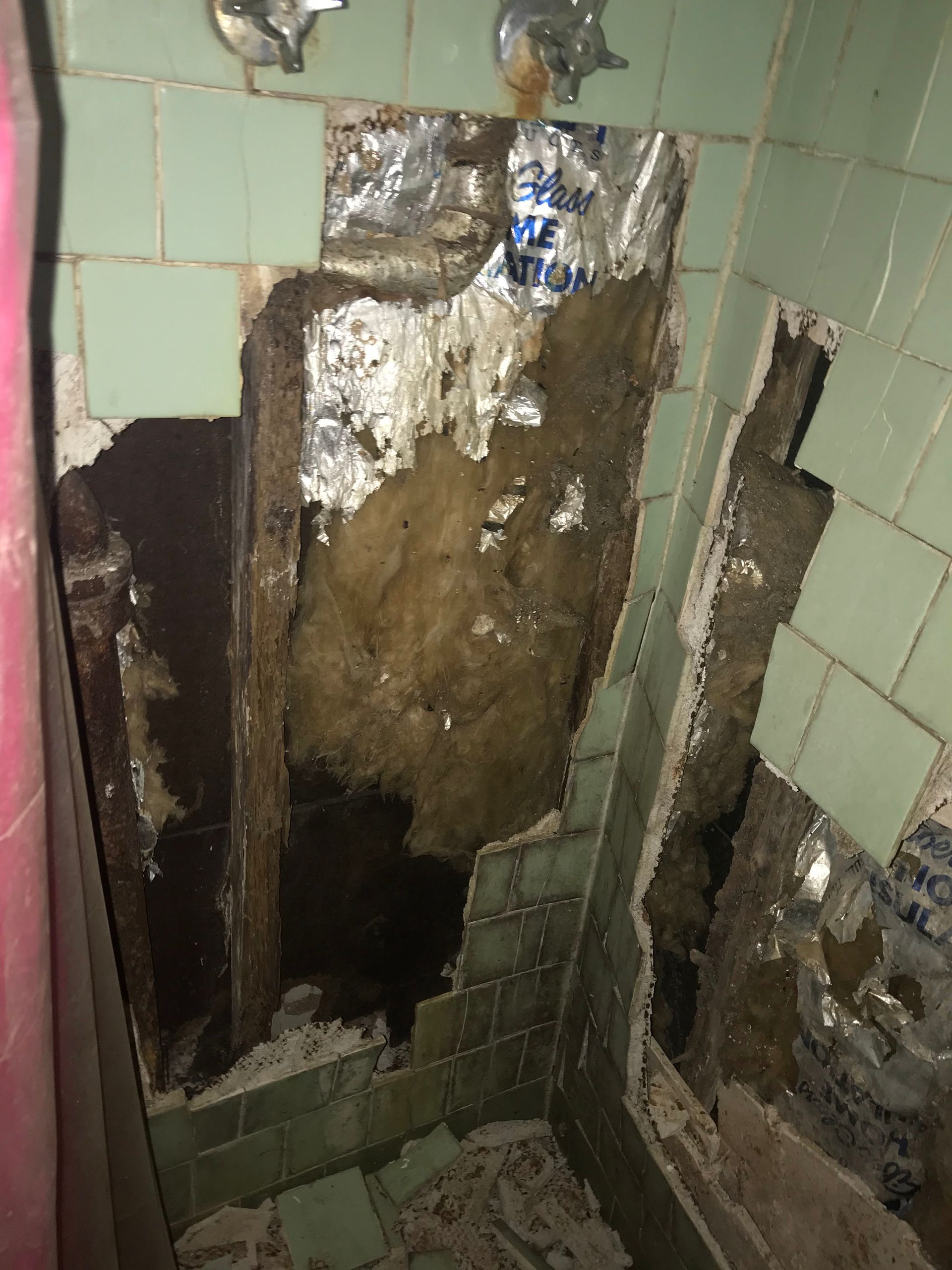A bathroom with a hole in the wall and a broken shower door.
