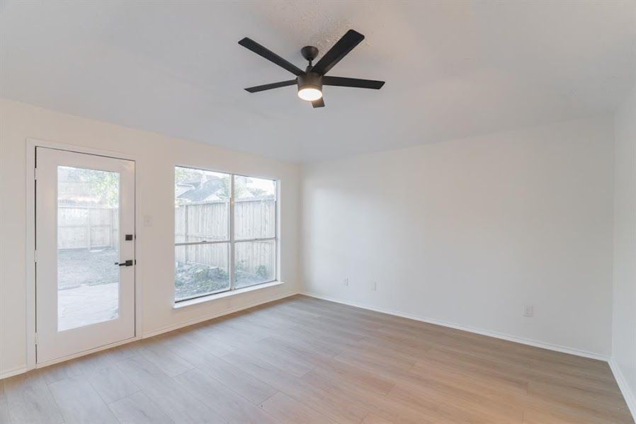 An empty living room with a ceiling fan and a door.