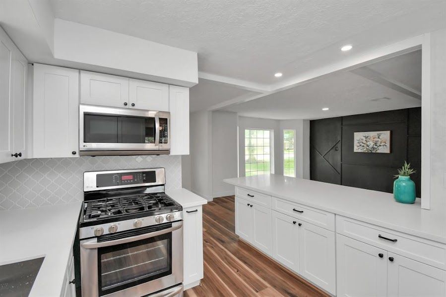 A kitchen with white cabinets , a stove and a microwave.