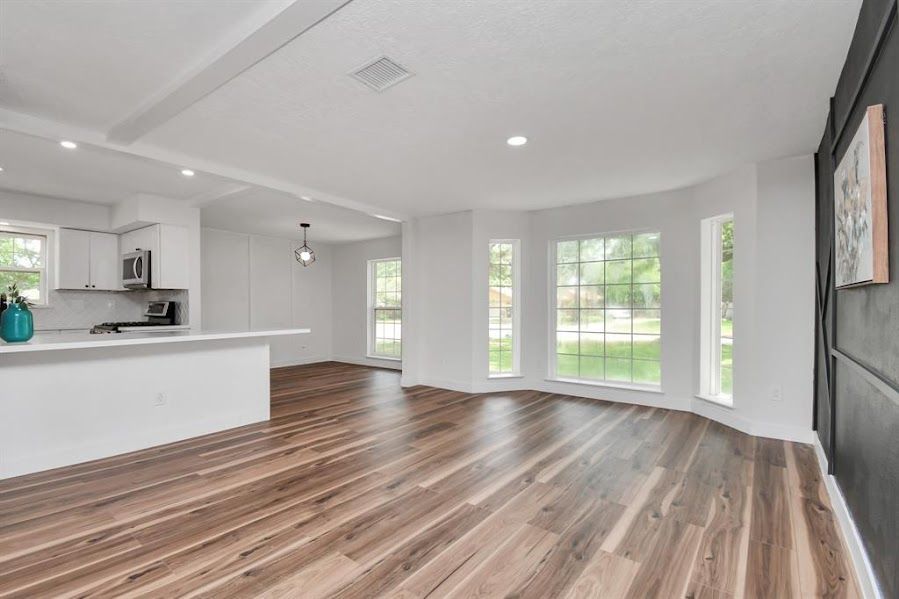 A living room with hardwood floors and a kitchen in the background.