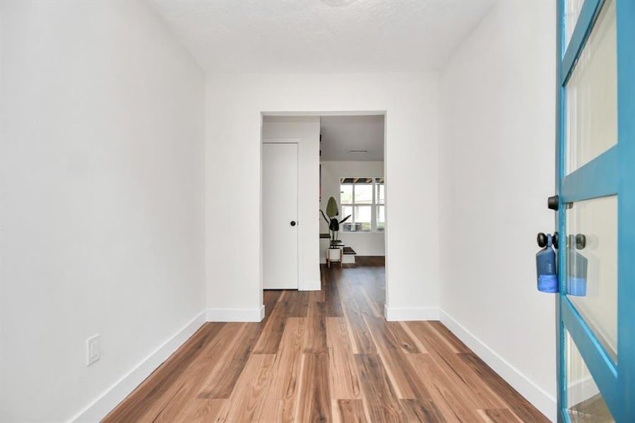 A hallway with hardwood floors and a blue door leading to a living room.