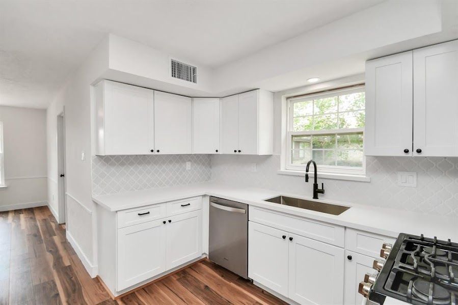 A kitchen with white cabinets , a sink , a stove , and a window.