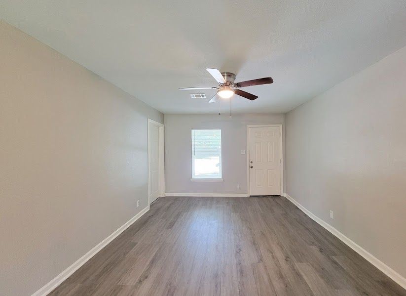 An empty living room with a ceiling fan and a window.