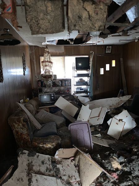 A living room with a lot of broken furniture and a ceiling that is missing