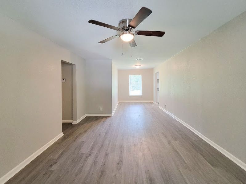 An empty living room with hardwood floors and a ceiling fan.