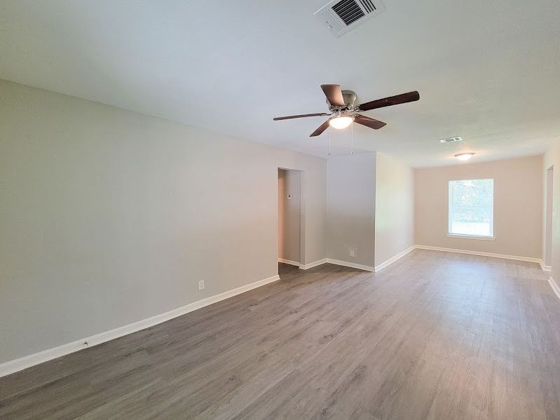An empty living room with a ceiling fan and a window.