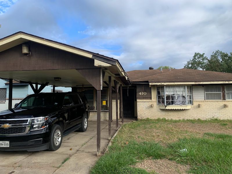 A black suv is parked under a carport in front of a house.