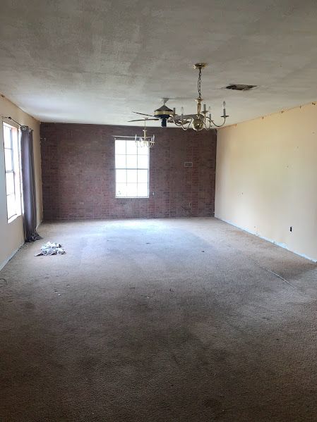 An empty living room with a ceiling fan and a brick wall.
