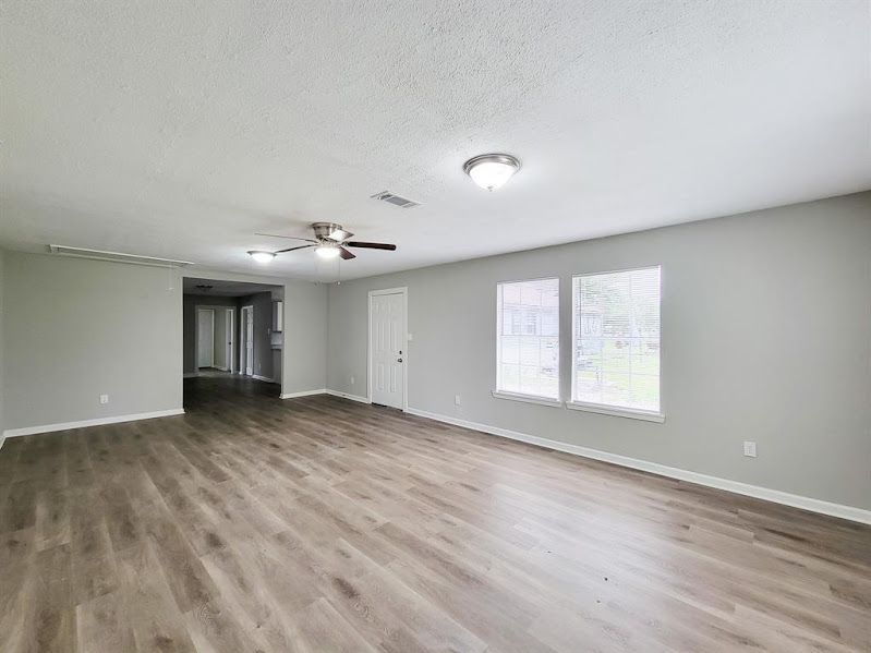 An empty living room with hardwood floors and a ceiling fan.