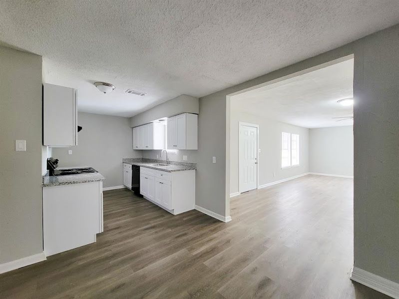A kitchen and living room in an empty house with hardwood floors.