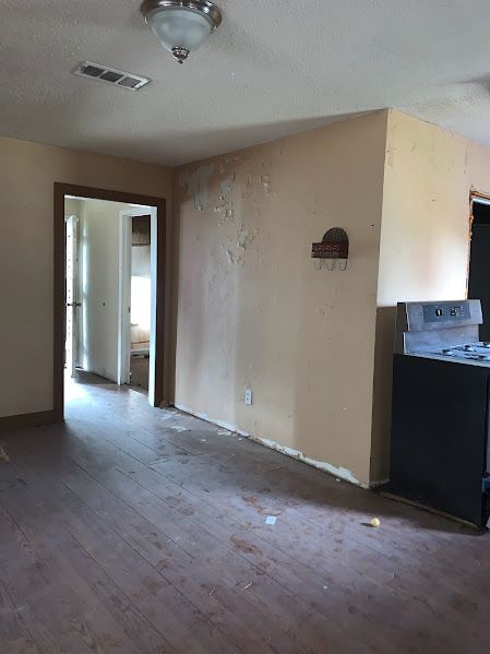 An empty living room with a stove and a doorway leading to a kitchen.