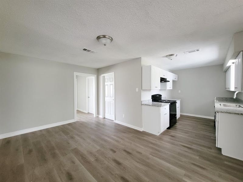 An empty living room with hardwood floors and a kitchen.
