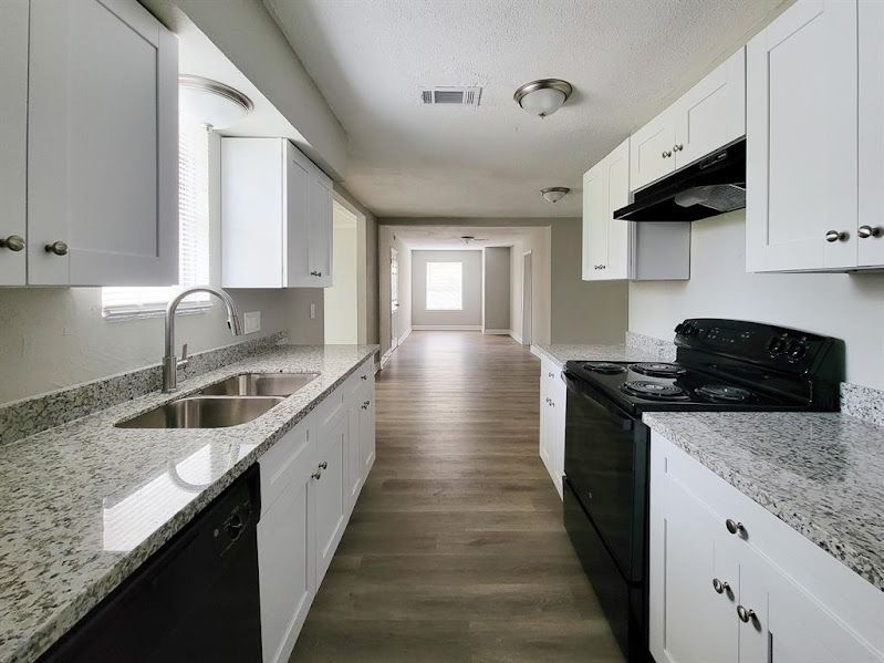 A long kitchen with white cabinets and granite counter tops