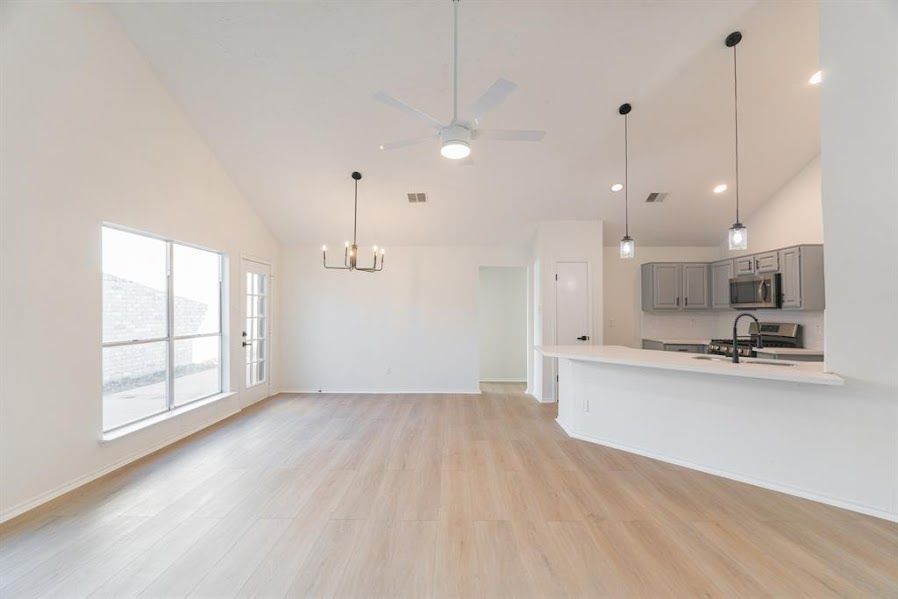 An empty living room with hardwood floors and a kitchen in the background.